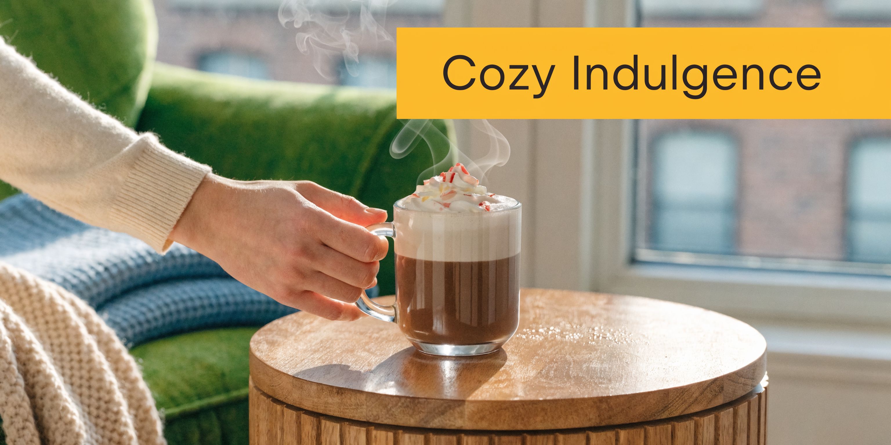 A person holding a glass mug of steaming hot peppermint mocha coffee while relaxing in a chair.